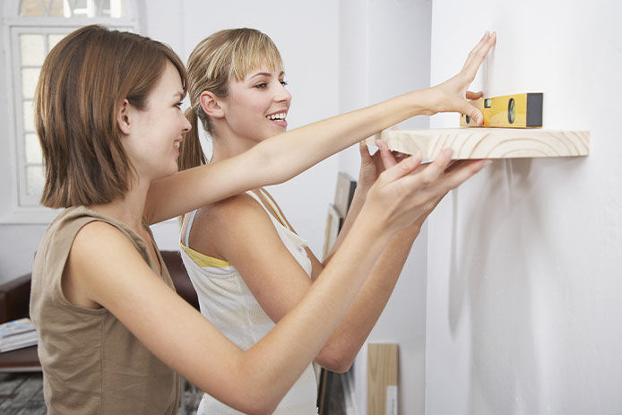 Two women leveling a floating shelf