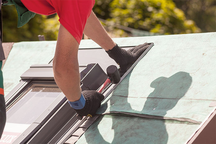 A professional installing saddle flashing on the top of a newly installed skylight 
