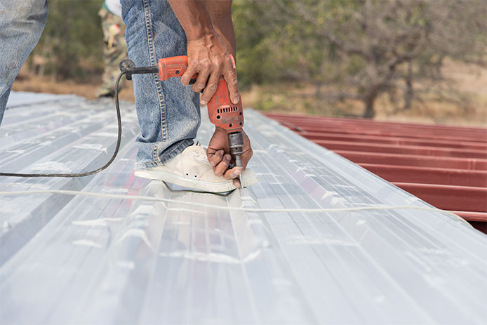 A professional installing a silver metal roof with a drill kit and screws. 