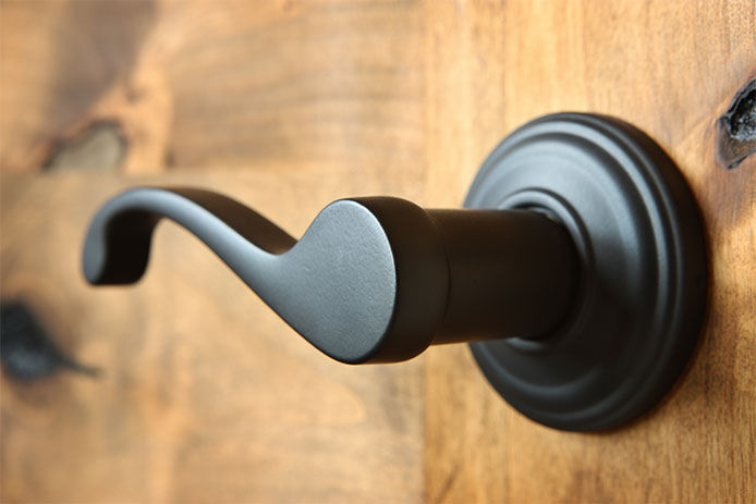 Doorknob - lever styled handle - matte black finish - on solid knotty alder wood door.