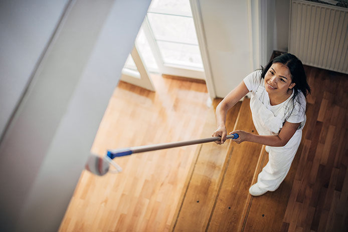 A woman painting a ceiling with a roller extender