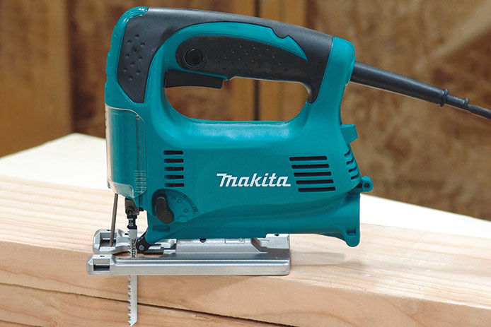 A lifestyle image of a Makita jigsaw sitting on a stack of lumber in a wood shop