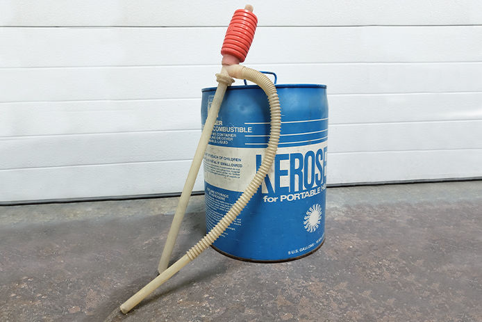 A siphon pump leaning on a blue can of kerosene