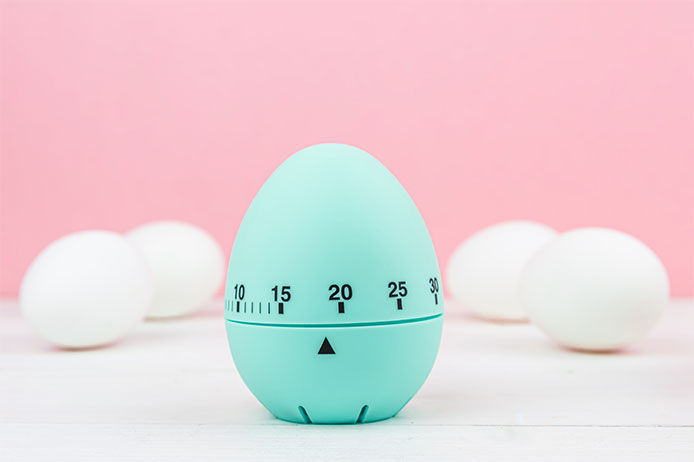 A teal egg timer with eggs against a pink background 