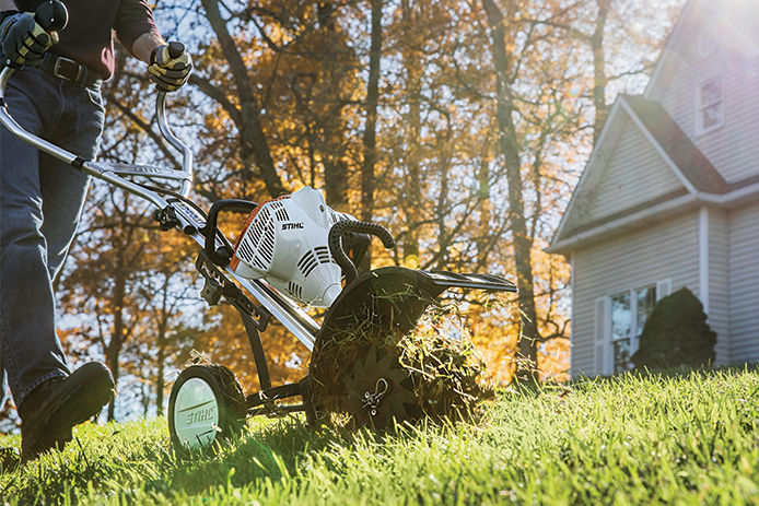 Man pushing a Stihl dethatcher across the yard