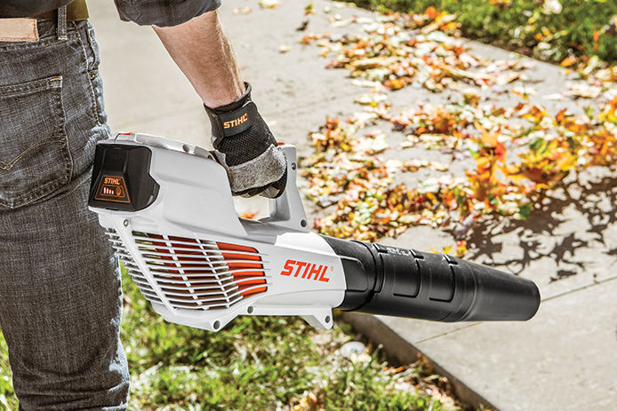 Man with a Stihl leaf blower in his hand blowing leaves off of a sidewalk