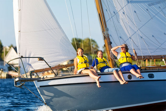 Grandmother, daughter and granddaughter enjoy a day of sailing while wearing life jackets