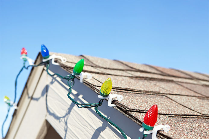 Close-up detail portion of a long string of LED Christmas lights clipped to a house roof. The LEDs are housed within faceted plastic covers which replicate the look of incandescent bulbs. LEDs last longer and are much more efficient than conventional bulbs.