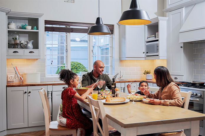 A family at the dinner table eating with kitchen lights on.