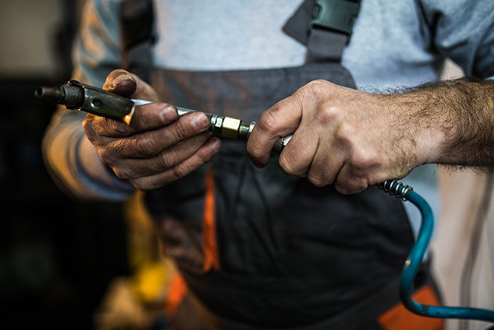 Man with greasy hands holding air tool connected to compressor