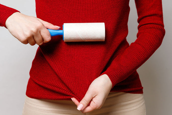 Woman using a lint roller on her red long sleeve shirt