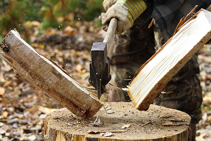 Person wearing work gloves in the action of splitting wood with an axe
