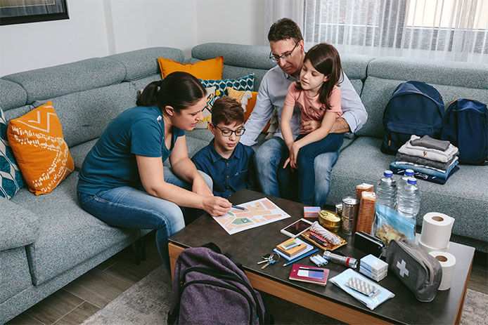 A family surrounding coffee table looking at an evacuation plan with to-go supplies on the table
