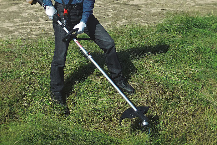 Makita brush cutter attachment being used to trim back tall grass