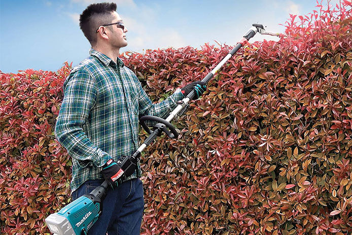  Man using Makita hedge trimmer attachment on the Makita Couple Shaft tool to trim back hedges