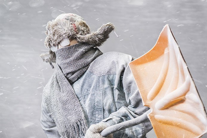 Man bundled up in the blowing snow carring a yellow shovel