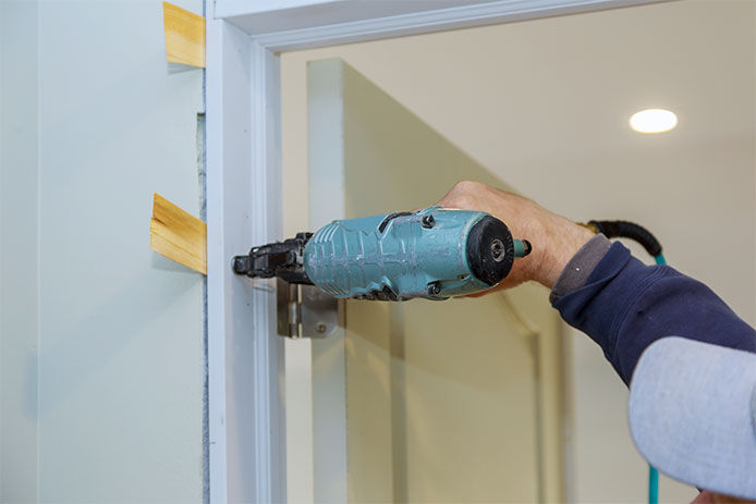 A close up image of a professional using a framing nail gun to install a prehung door into the door jam. 