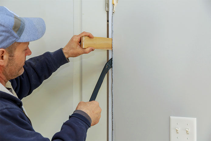 A professtional using a crow bar to install wood shims in the door jam of a prehung door 