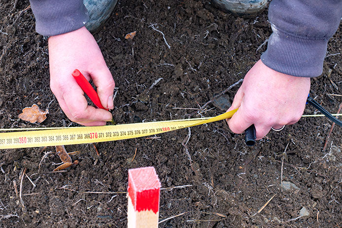 A persom using a yellow tape measure to measure out the layout of a playground set