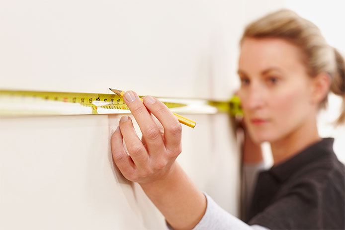 Woman with tape measure stetched against the wall about to mark for the hanger