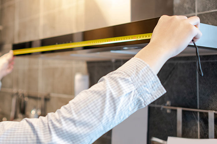 Person using a tape measure to measure the dimensions of their range hood