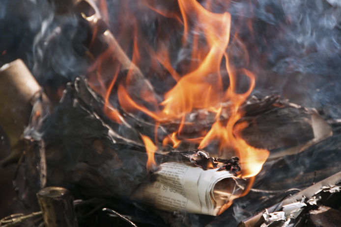 A newspaper roll is shown burning in a smoky fire. Orange flames are creating a great deal of smoke. 