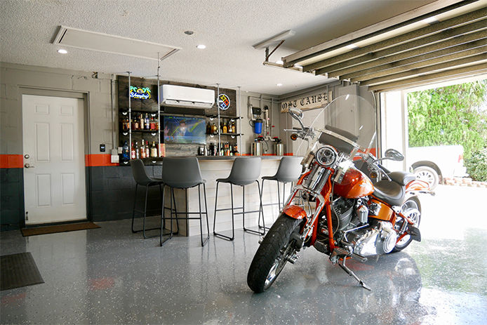 A beautiful orange and black motorcycle sitting in a garage that also doubles as a bar and social space