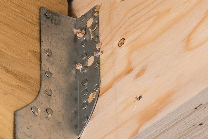 A close up of a metal corner bracket on wooden joists