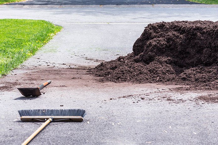 A pile of mulch in the driveway with a push broom