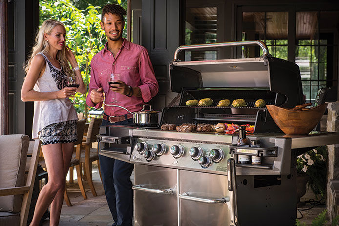 A young couple standing next to a Broil King propane grill cooking food for a BBQ