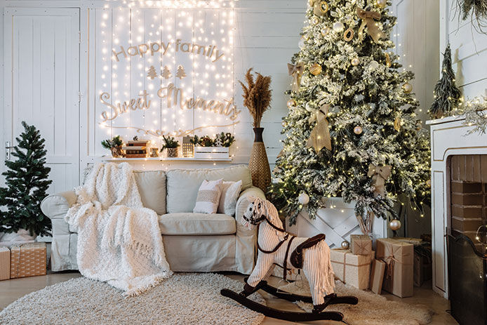 White flocked Christmas tree set up in a living room beside a fireplace and a rocking horse 