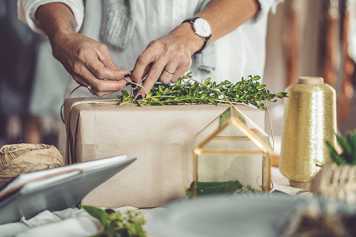 Woman tying a piece of green sprig to the top of a wrapped Christmas gift
