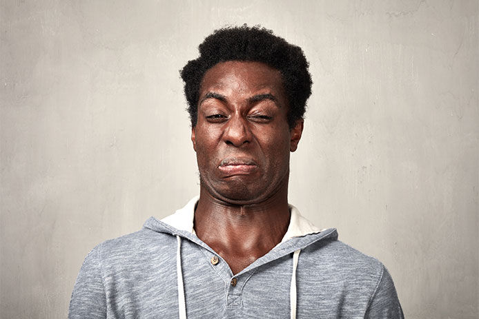 A middle age man wearing a gray sweat shirt making a fowl smelling face. 