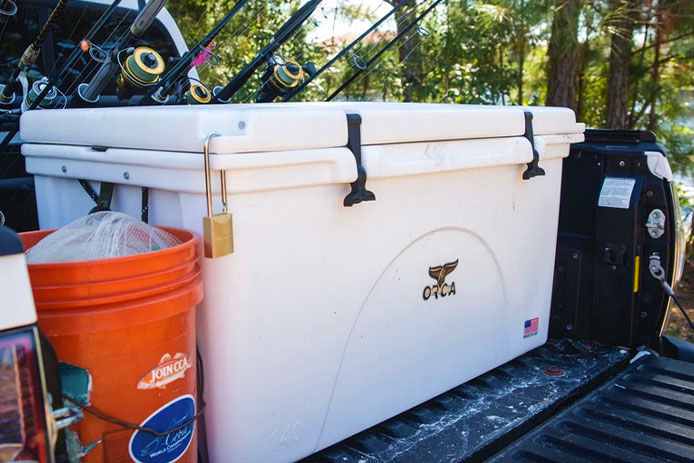 A white ORCA cooler in the bed of a pickup truck with fishing poles