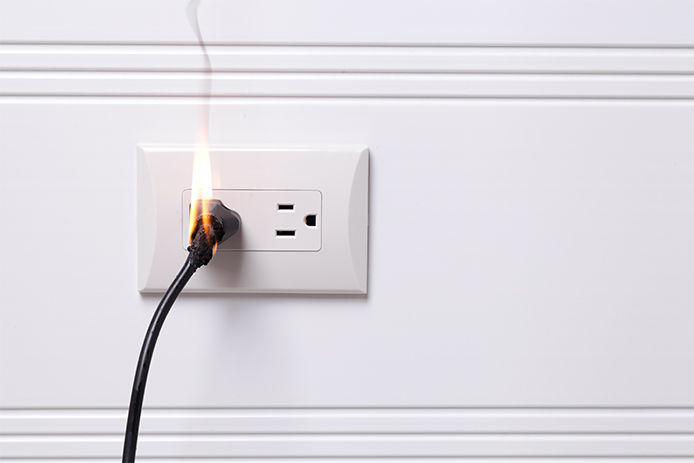 A power cord plugged into wall outlet that is on fire