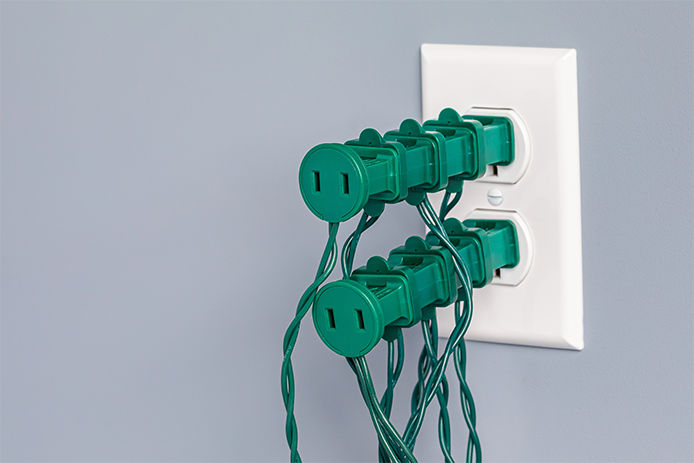 Multiple green Christmas light plugs plugged into on another in an outlet. 