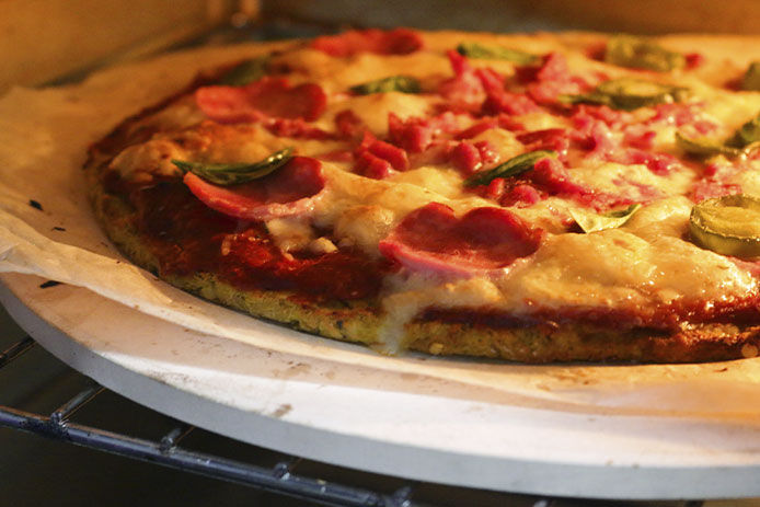 A pepperoni pizza on thin crust is cooking in a glowing oven atop a pizza stone.