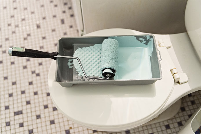 Paint roller and tray with a blue paint on the top of a toilet seat