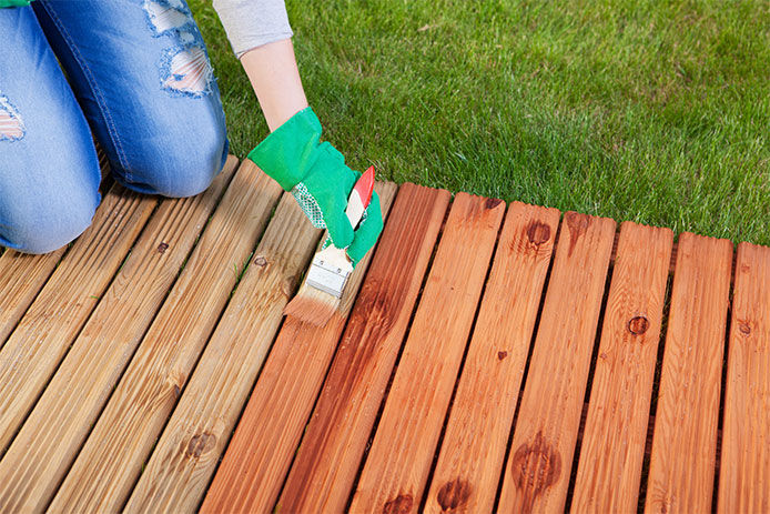 A person paiting a deck with a brush