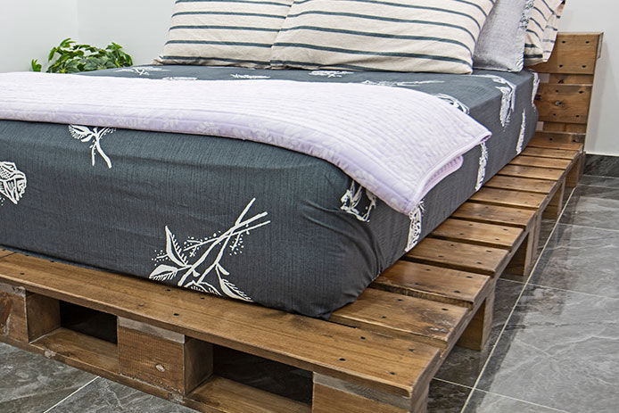 A made bed on top of a stained bed frame made from pallets