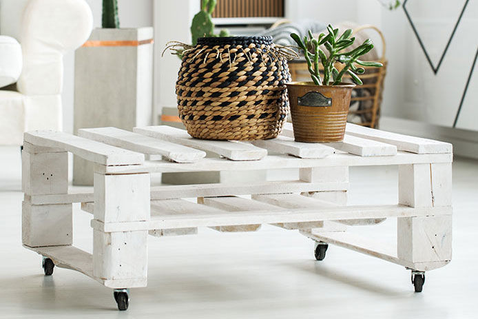 A white coffee table made of wood pallets with a couple plants on top of it in a living room