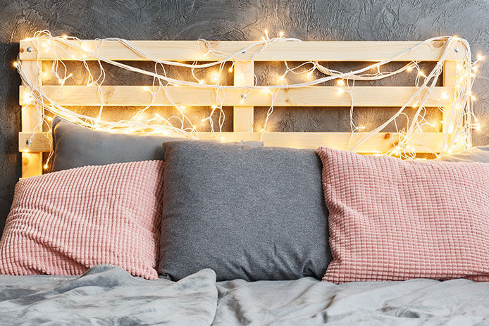 A bed headboard made from pallets strung with Christmas lights