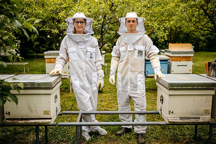 Two beekeepers in bee suits standing next to boxed beehives