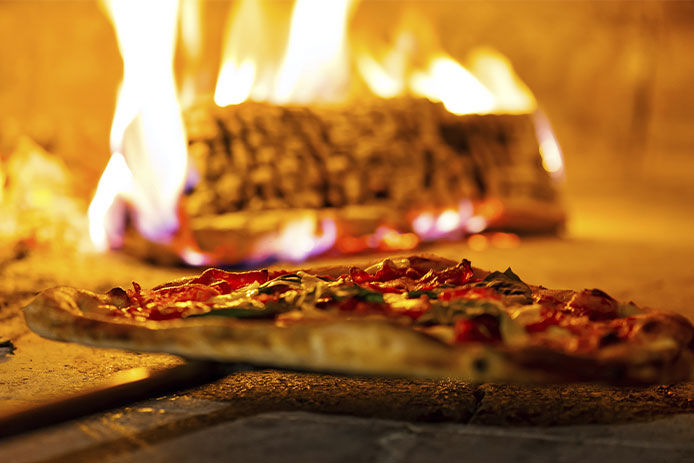 A well-cooked, bubbling pizza is shown against the flaming log of a pizza oven.