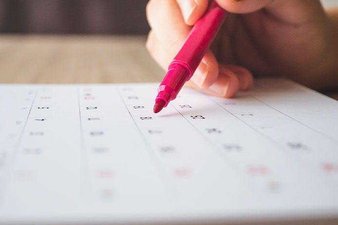 Hand with pen writing on calendar page closeup