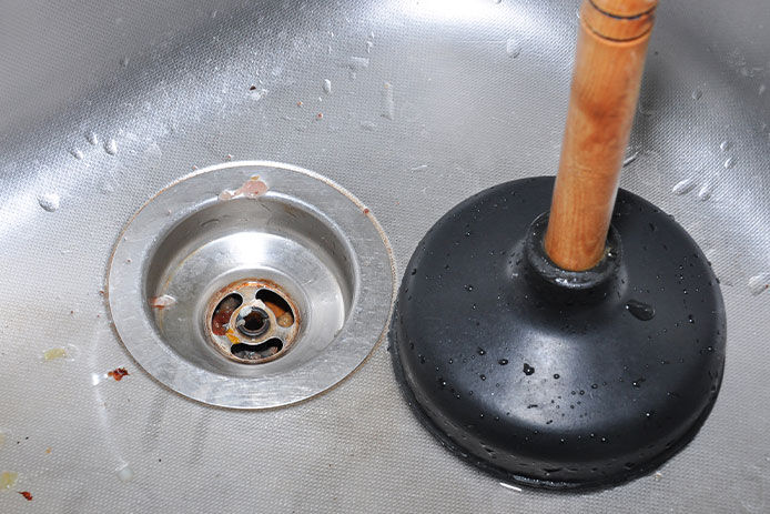 A plunger in the sink next to the sink drain