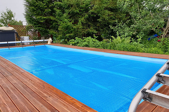 A blue pool cover, covering an inground pool next to a wooden deck for winter protection