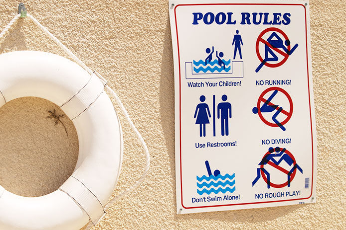 Pool safety rules hanging on a stucco wall next to a community swimming pool