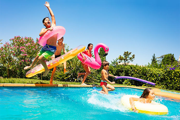 Group of age-diverse boys and girls, happy friends with swim floats jumping into swimming pool on the vacations