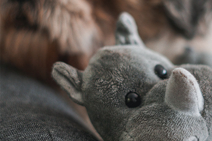 A close up image of a rhino stuffed animal sitting on a couch with a furry puppy in the background